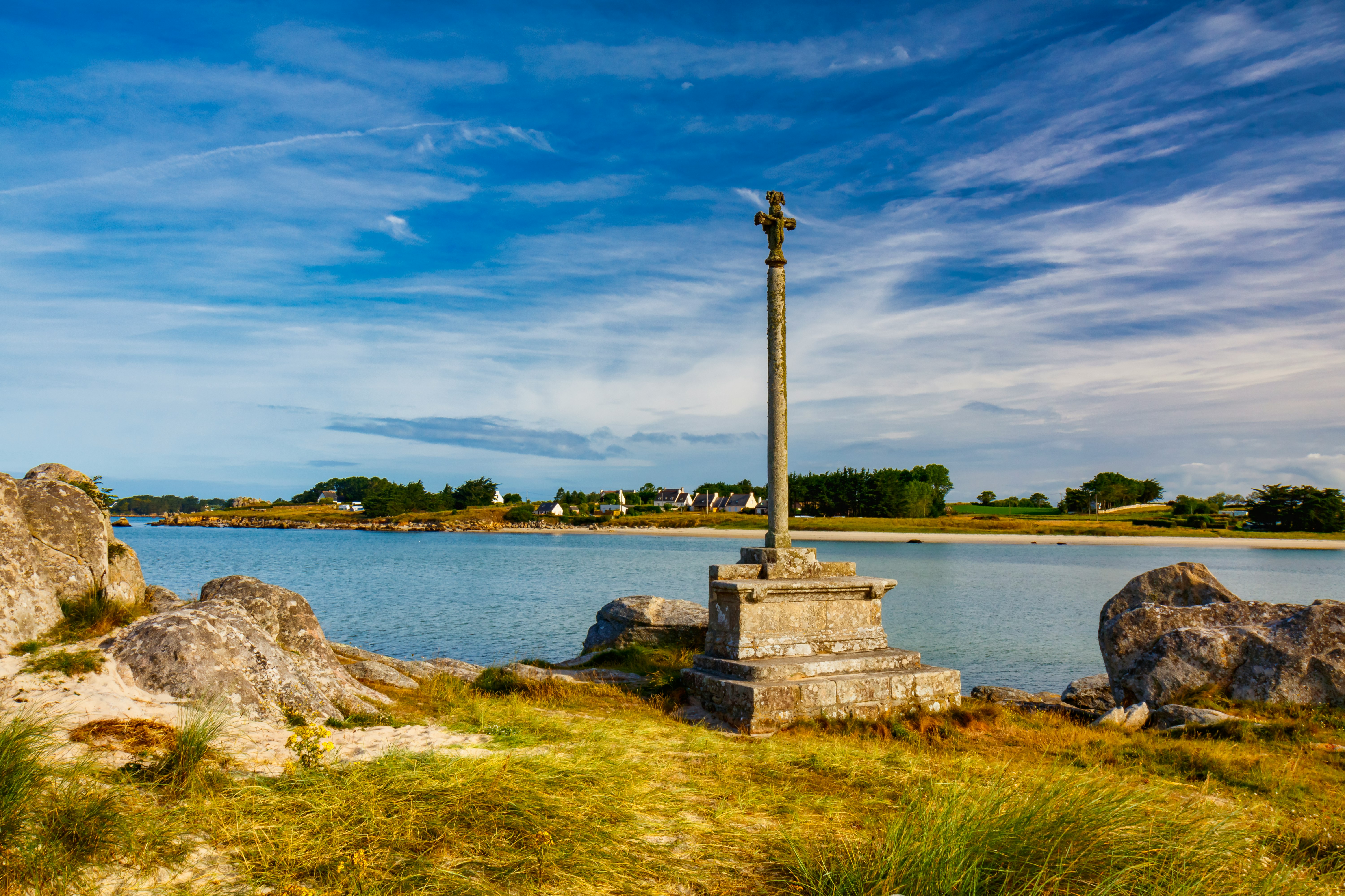 gray concrete cross on gray rock near body of water under blue sky during daytime